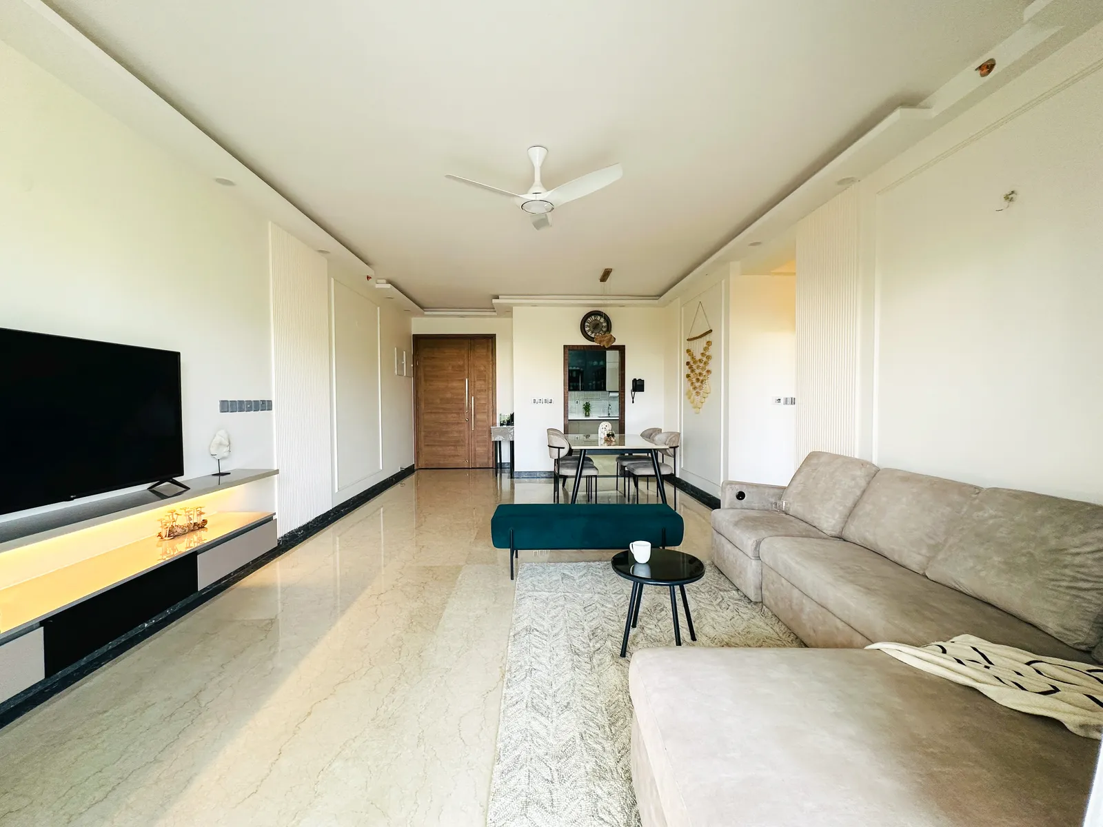 Long living room with TV unit, grey sectional and dining beyond — Somani's Residence
